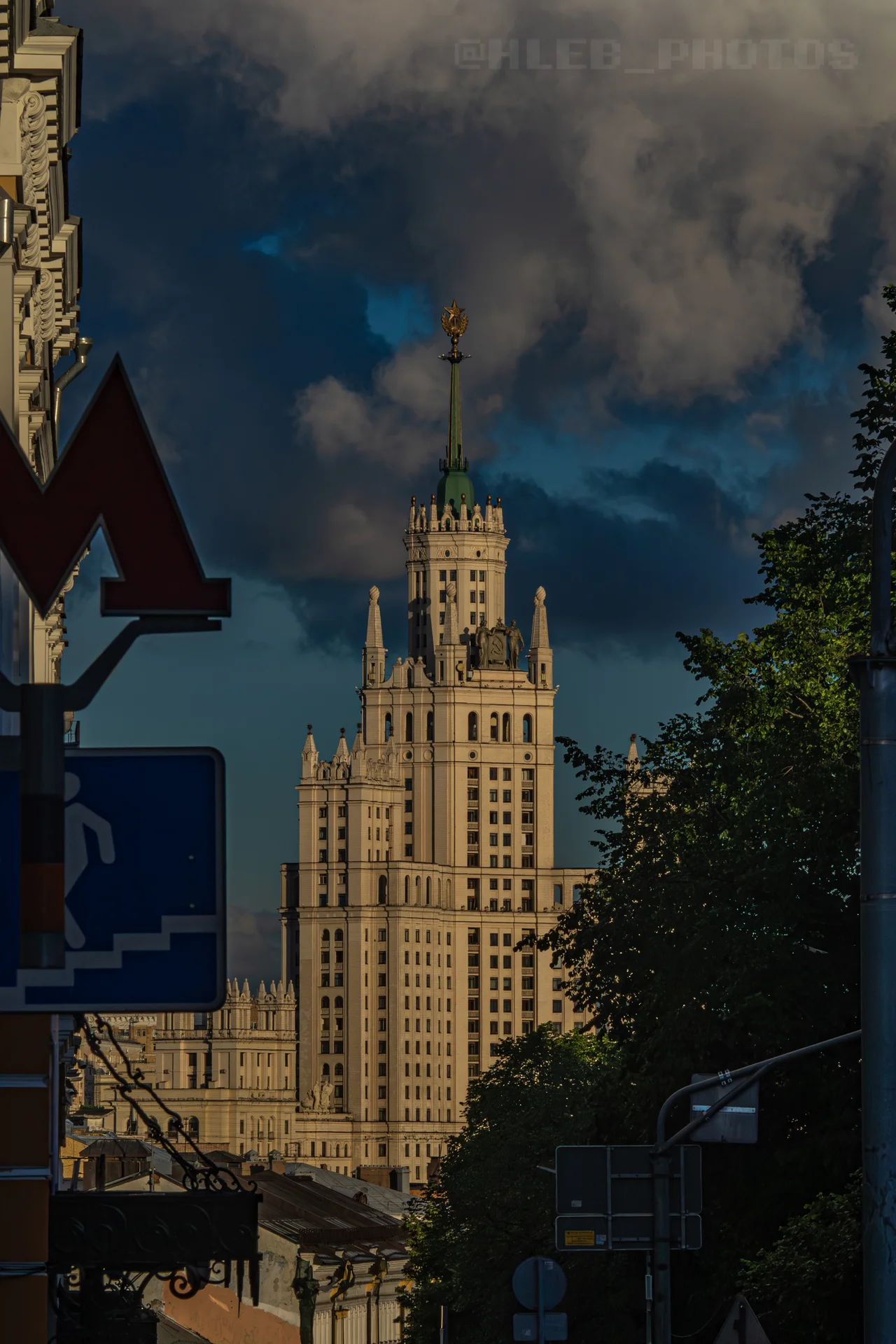 Крупный план сталинской высотки на Котельнической набережной в Москве, освещенной солнцем, на фоне темного грозового неба.