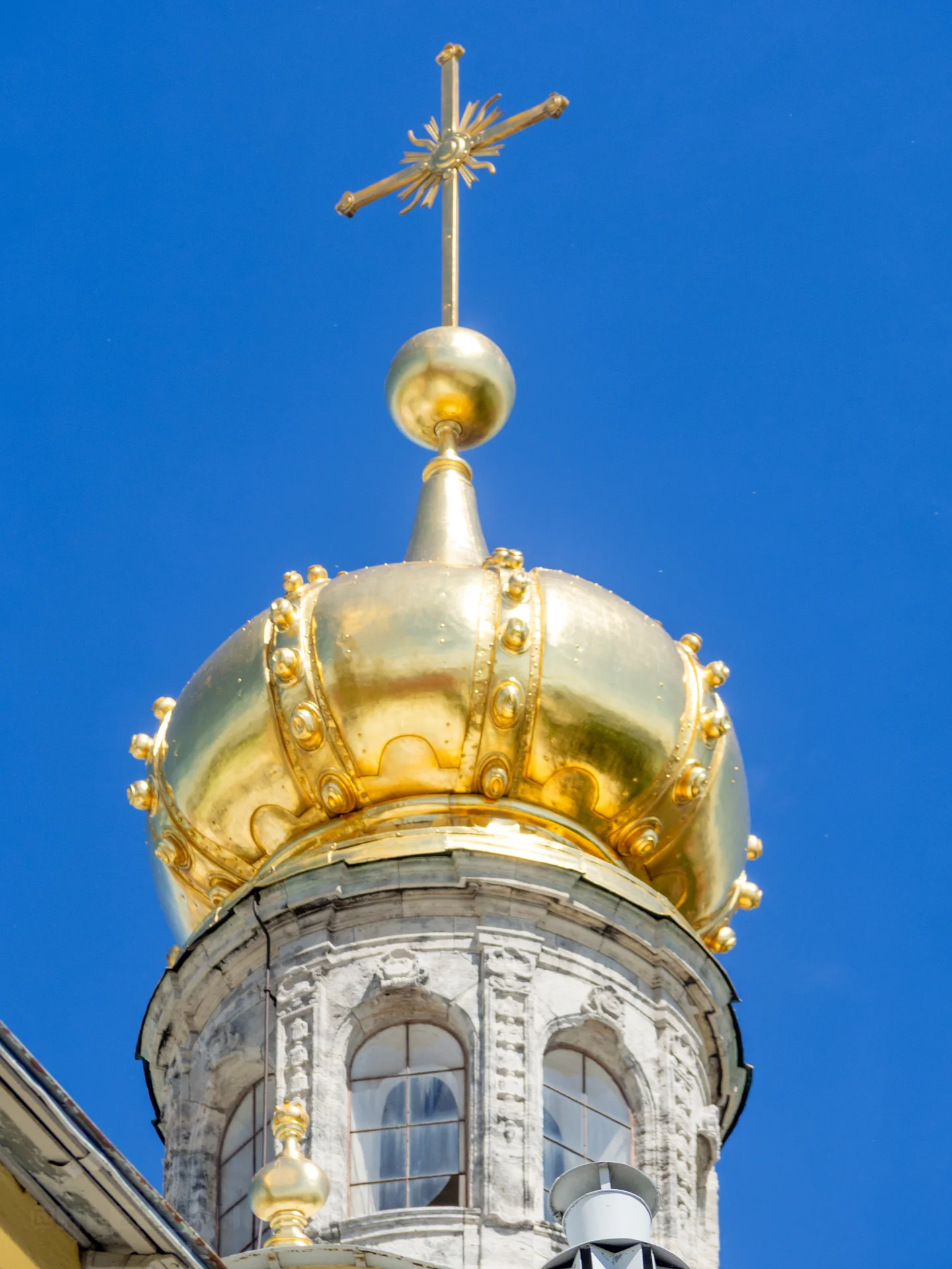Крупный план блестящего золотого купола со шпилем, крестом и декоративным узором на фоне неба.