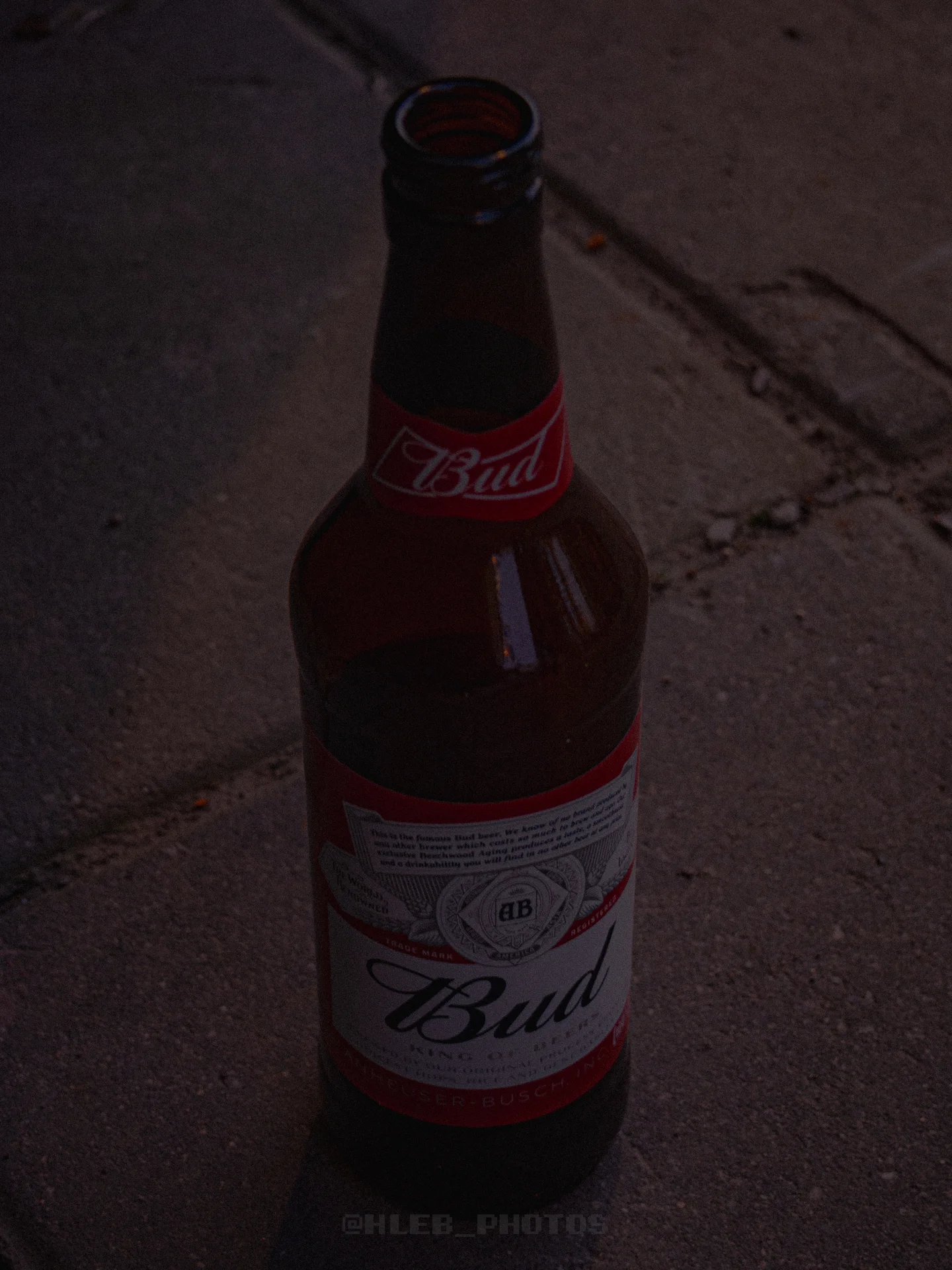 Стеклянная бутылка пива Bud на бетонном полу.
