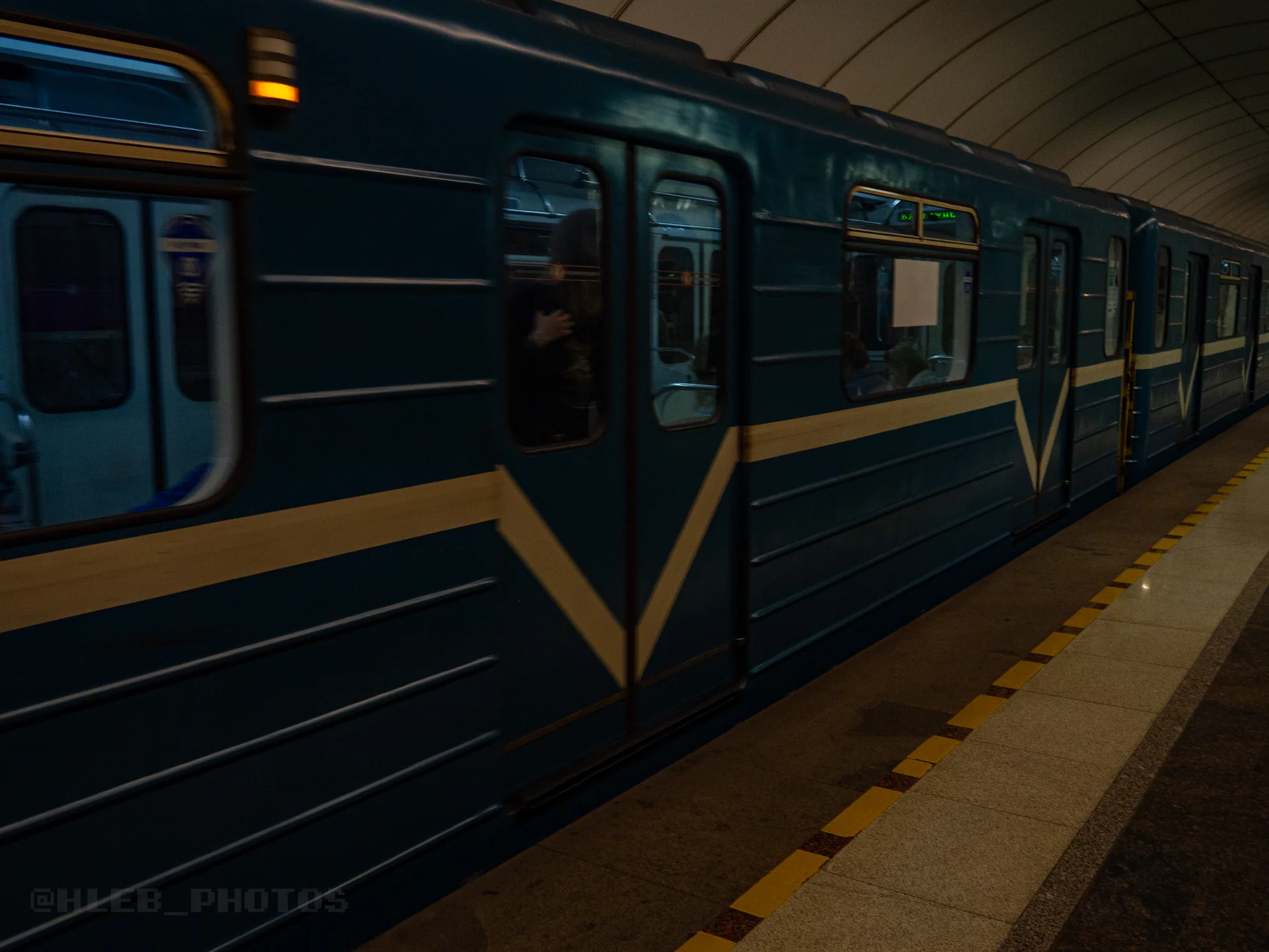 Синий вагон метро с белой полосой, стоящий у платформы станции с желтой ограничительной линией.