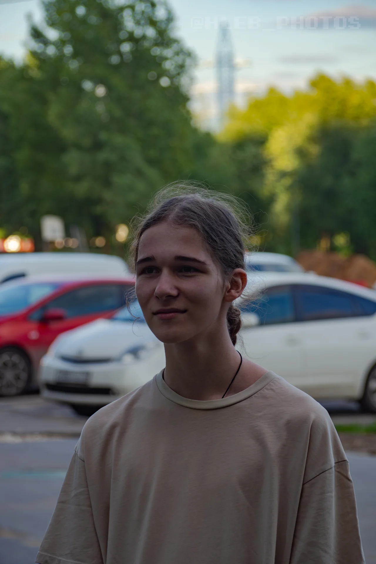 Портрет молодого человека в светлой футболке на улице на фоне припаркованных автомобилей.