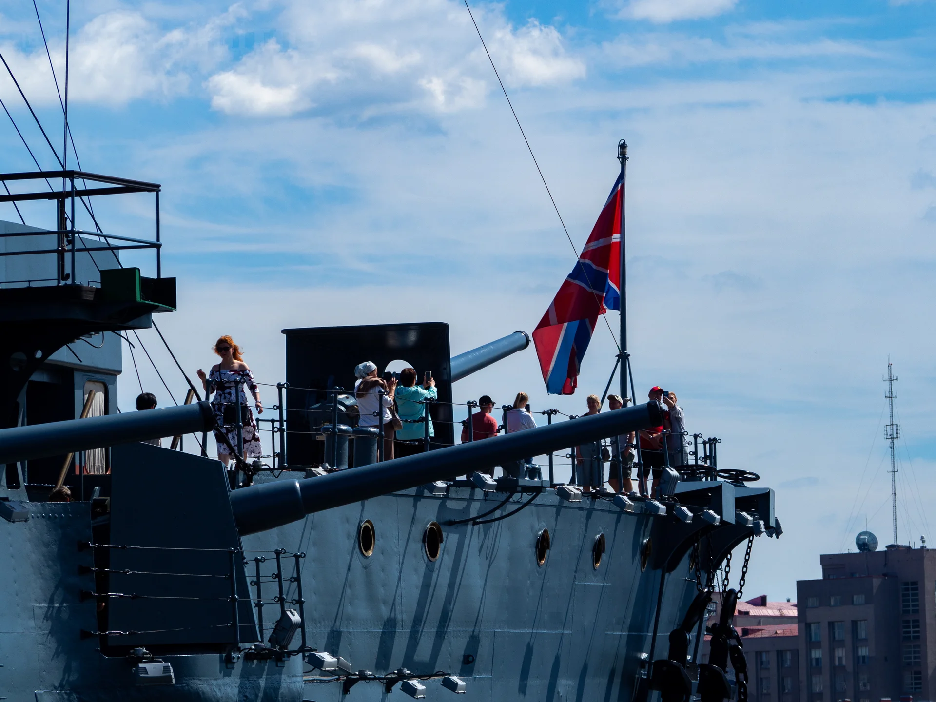 Группа людей на палубе военного корабля под развевающимся военно-морским флагом.