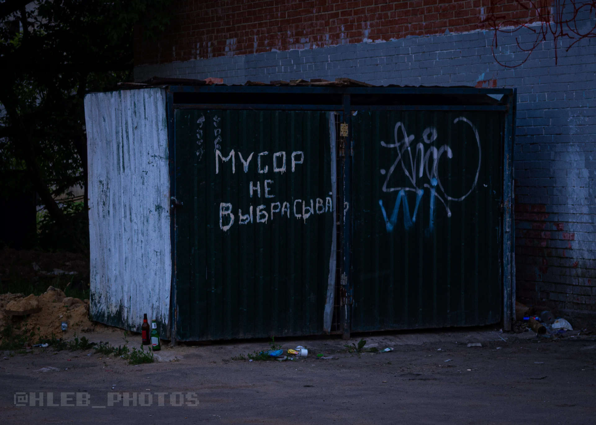 Темно-зеленый металлический мусорный контейнер с белой надписью краской «Мусор не выбрасывать».