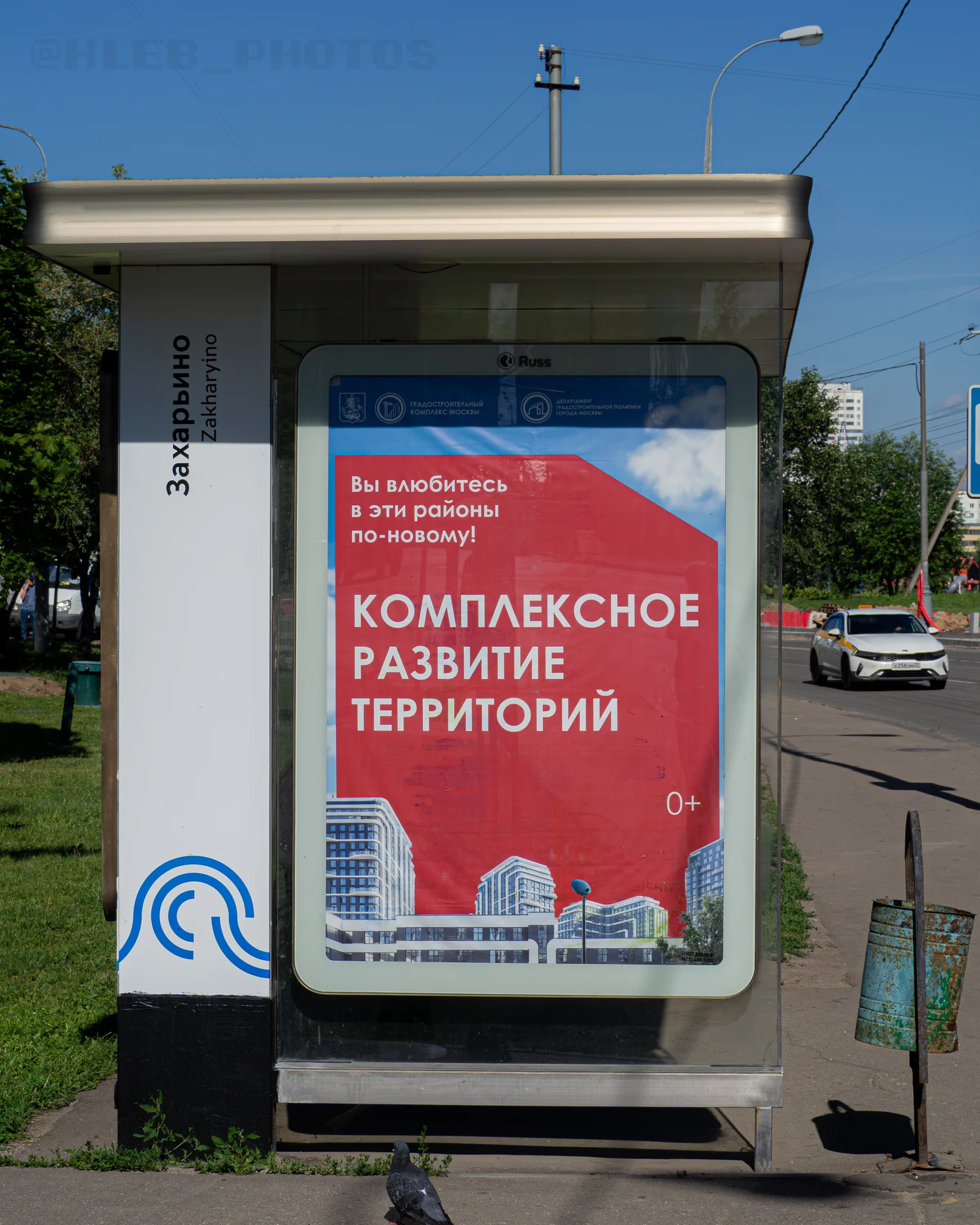 Автобусная остановка «Захарьино» с рекламным плакатом о комплексном развитии территорий и ржавая мусорка.