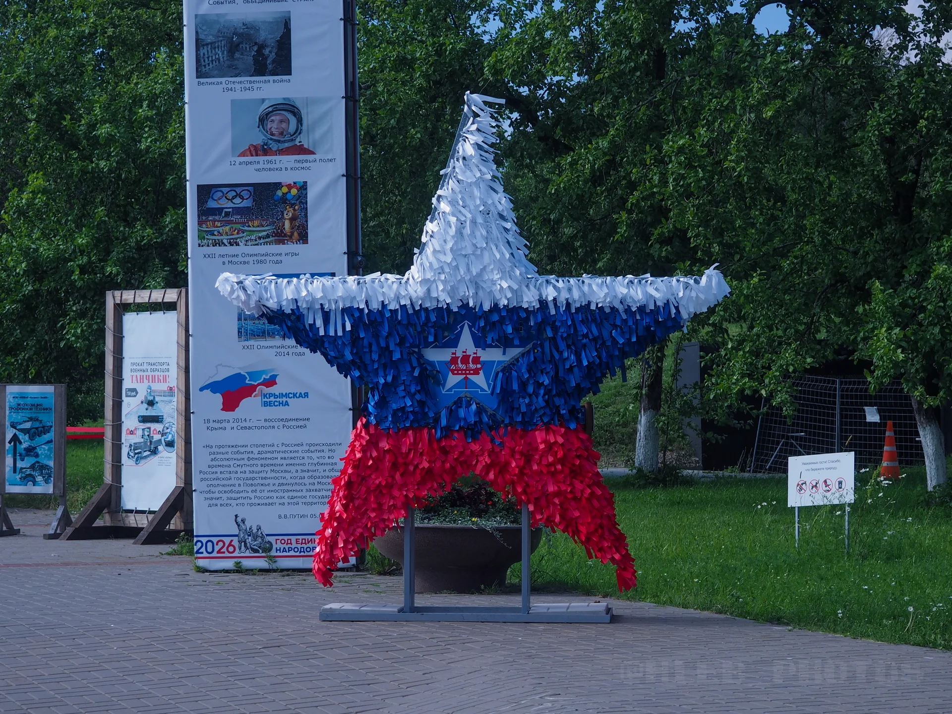 Большая декоративная звезда из синих, белых и красных полос на металлическом каркасе, установленная на пешеходной аллее парка.
