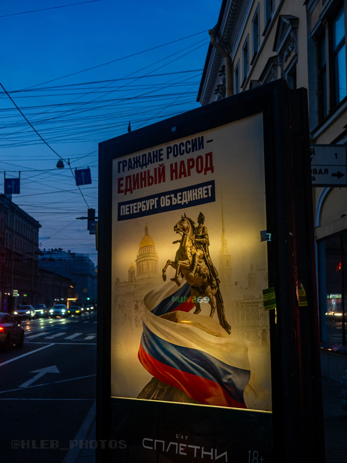 Светящийся городской билборд с патриотическим плакатом, изображающим памятник Петру I на фоне вечернего неба.