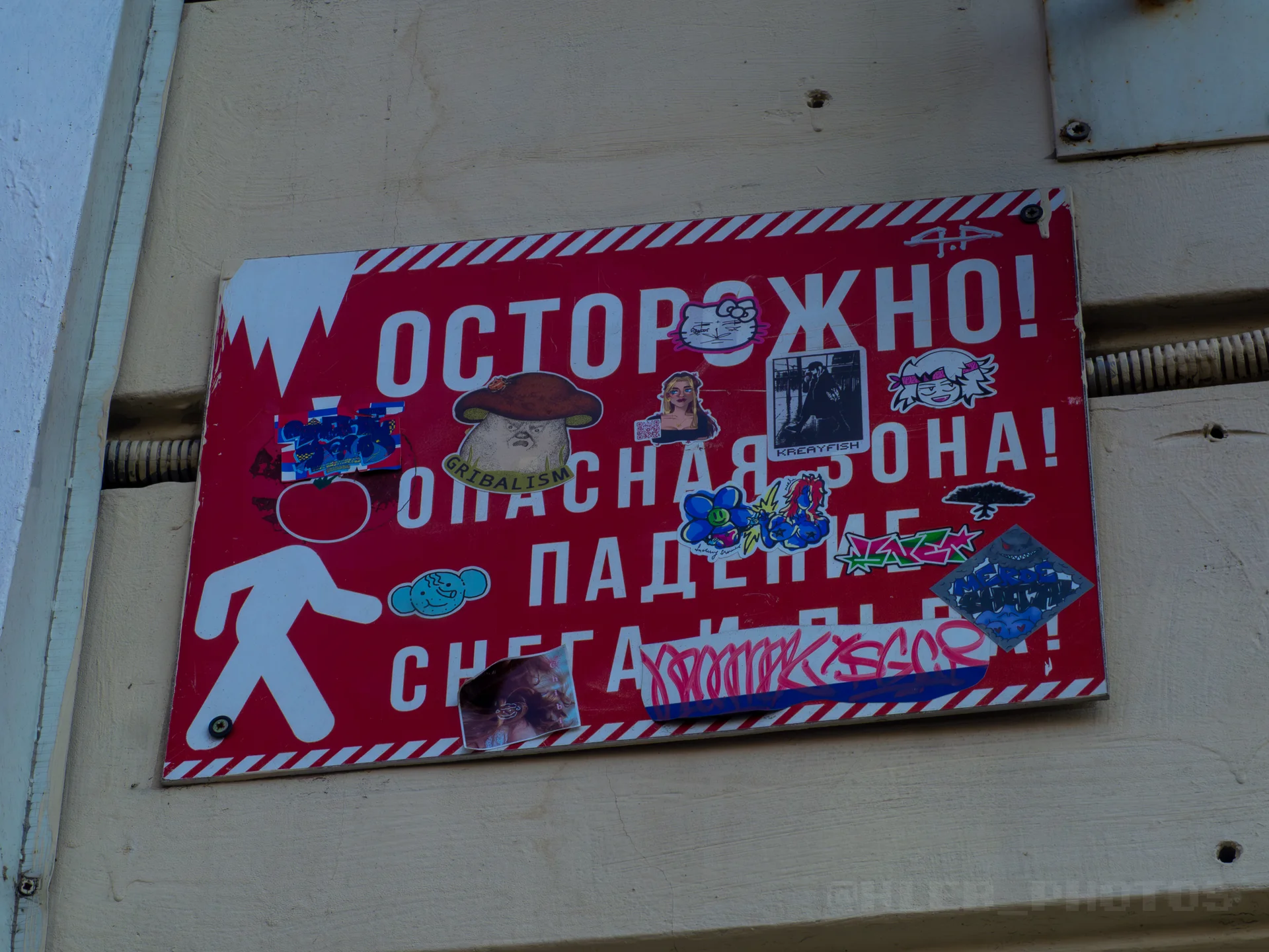Предупреждающая табличка «Осторожно! Опасная зона! Падение снега!», обильно обклеенная разнообразными стикерами и граффити.