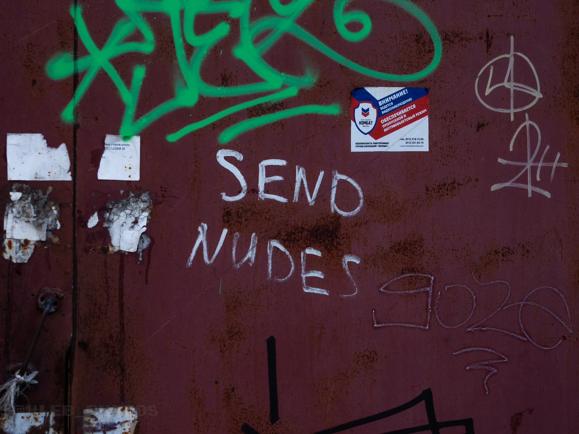Надпись белой краской «SEND NUDES» и другие теги на темной металлической поверхности.