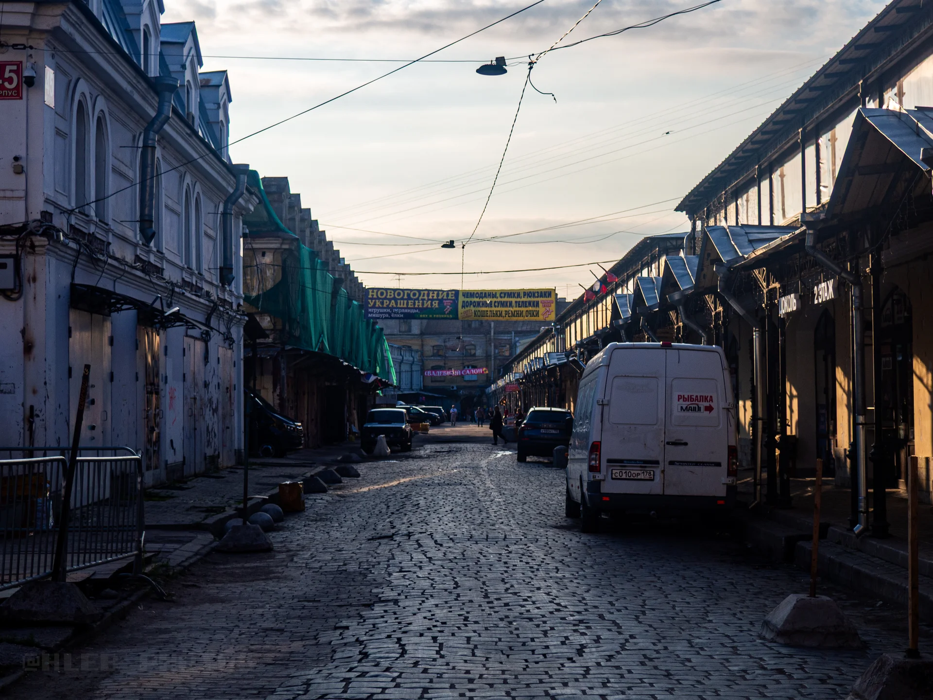 Узкая городская улица, вымощенная брусчаткой, с припаркованным белым фургоном в сумерках.