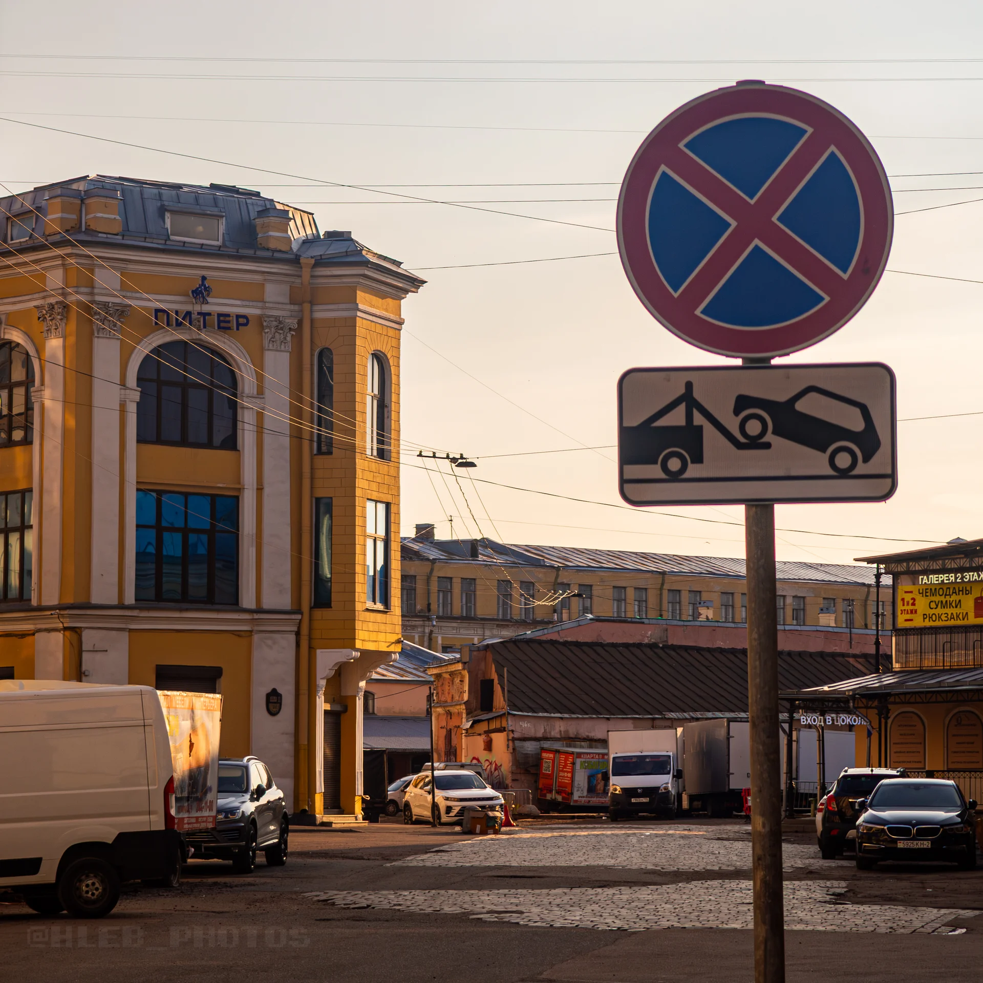 Перекресток с желтыми зданиями, припаркованными машинами и дорожным знаком «Остановка запрещена» на столбе.