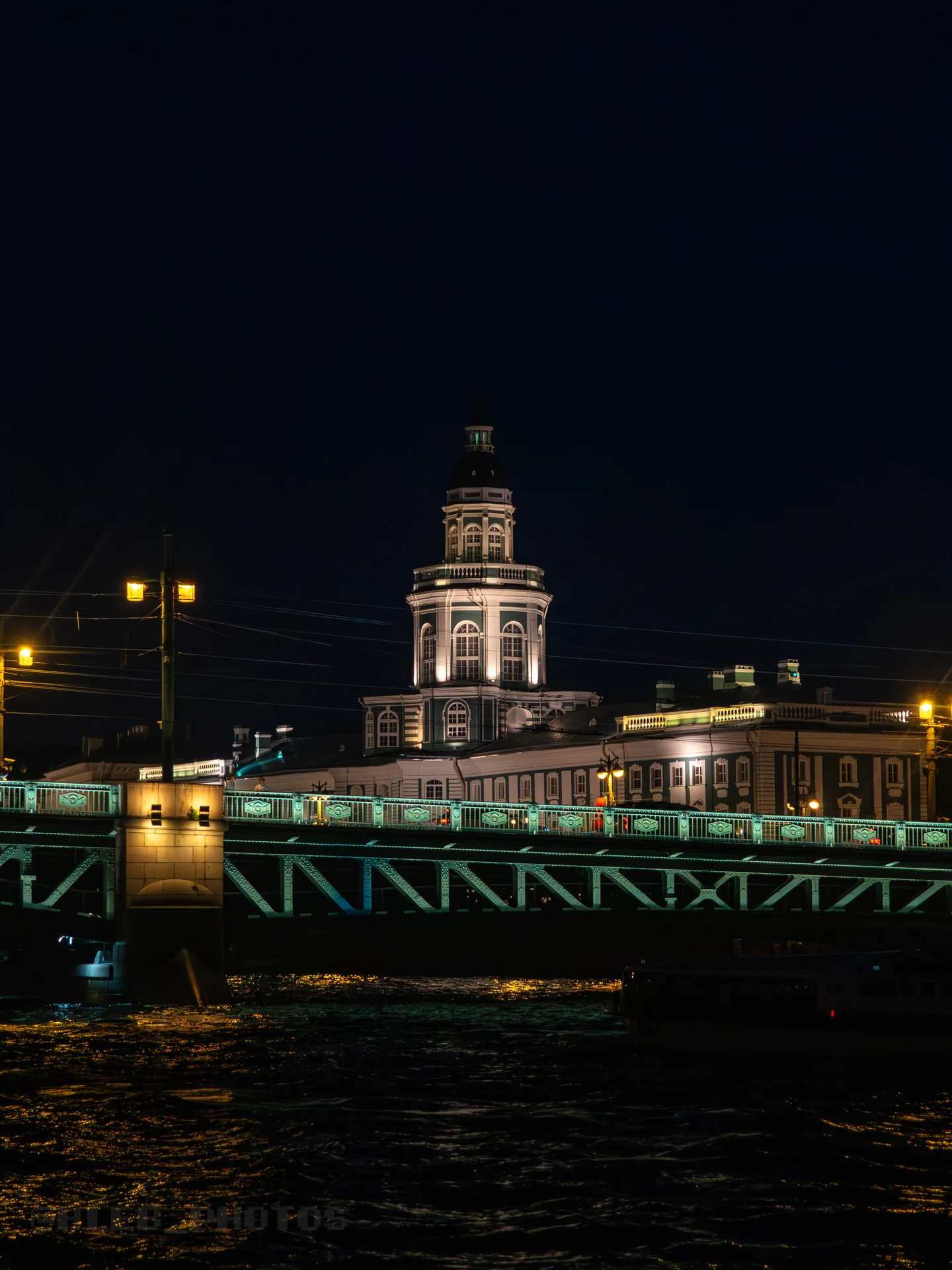 Подсвеченный мост и башня со шпилем в ночном городе на фоне темного неба.