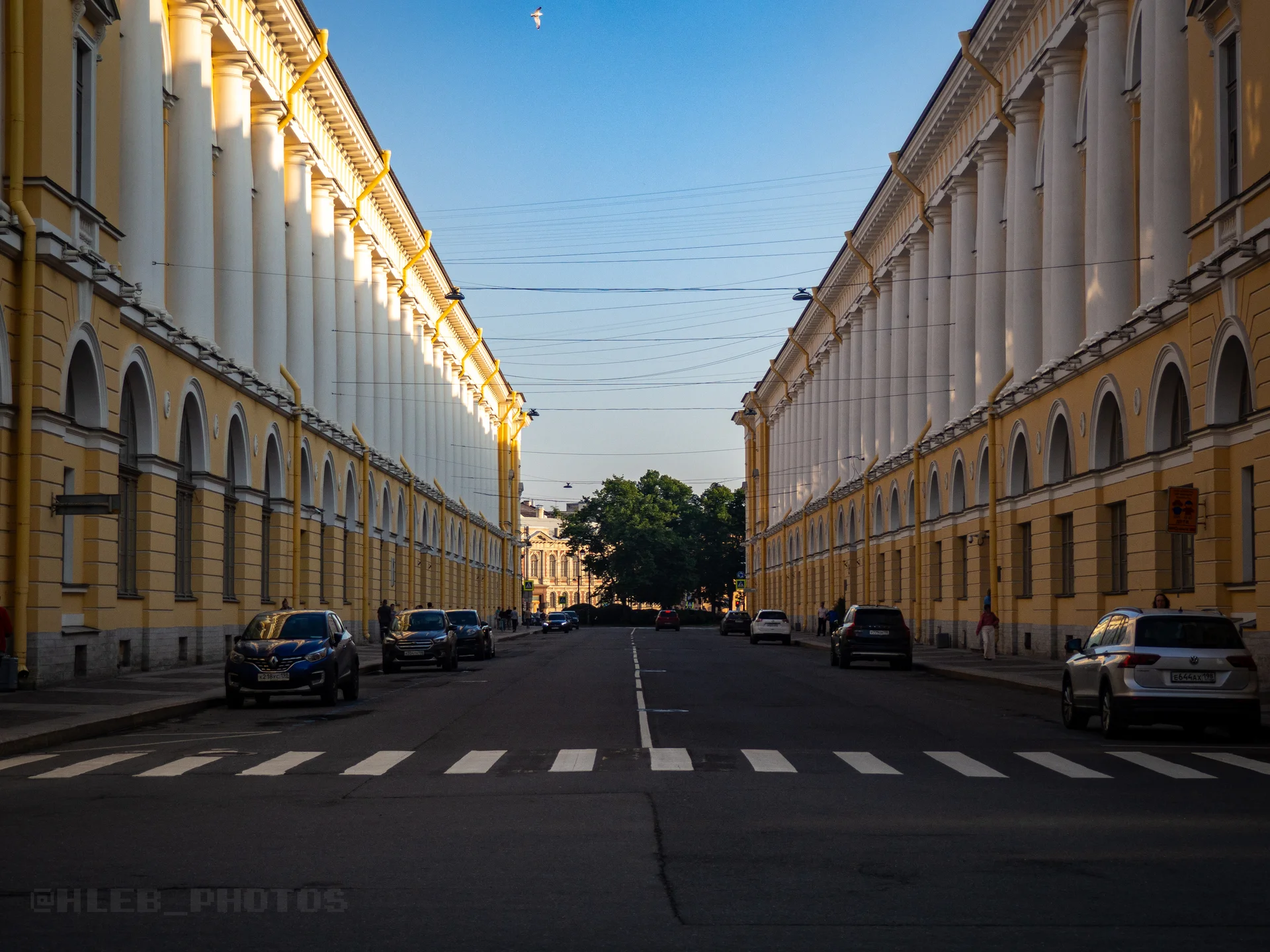 Прямая городская улица с пешеходным переходом и желтыми зданиями по обеим сторонам в солнечный день.