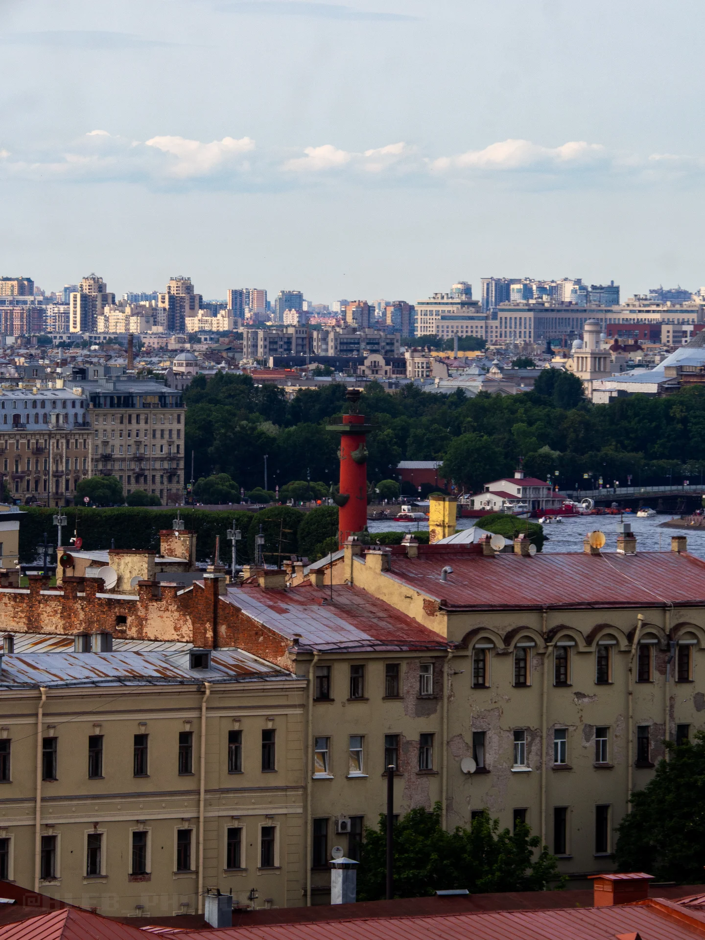 Вид сверху на черепичные крыши исторического центра города и красную колонну на заднем плане.