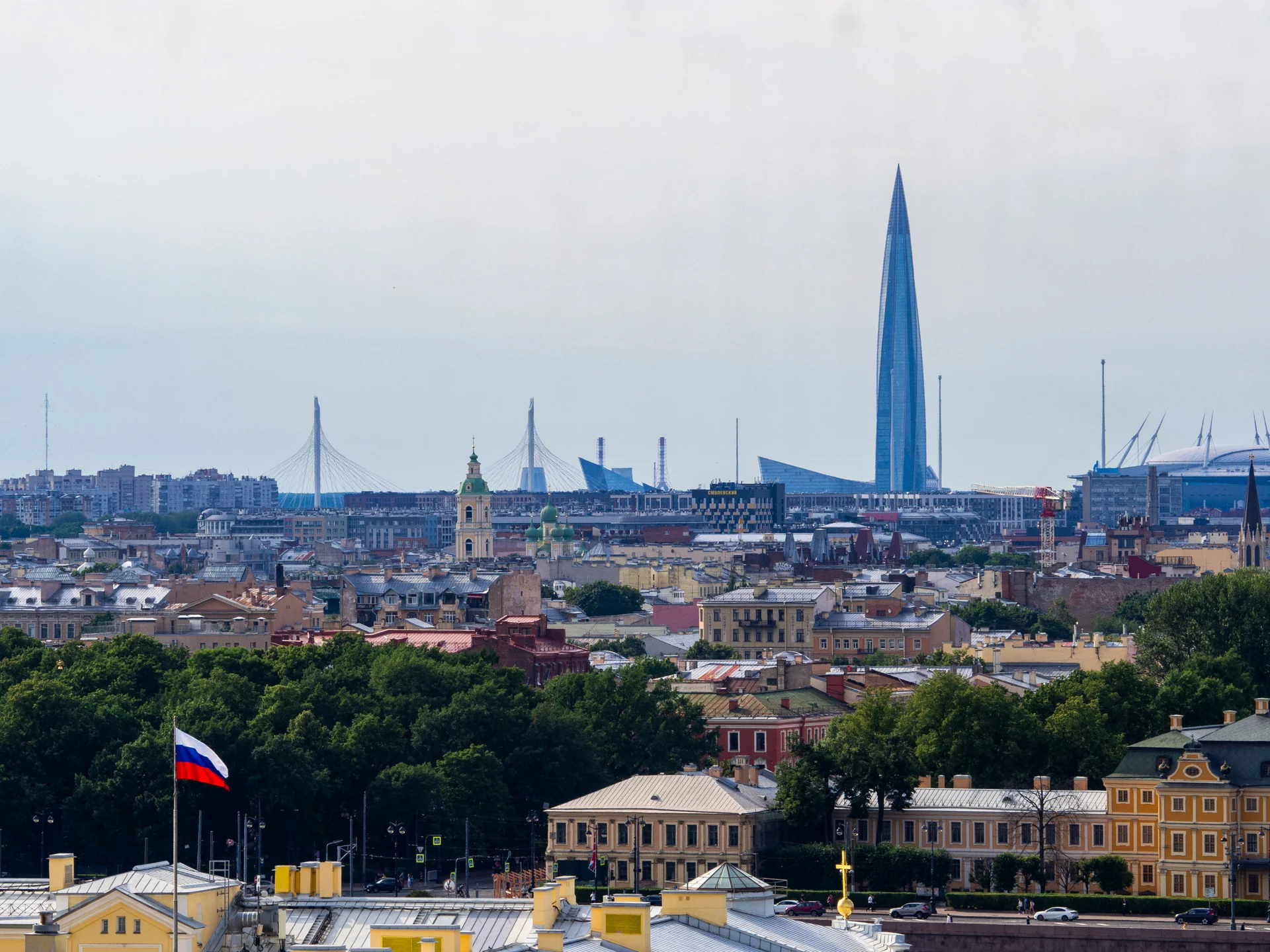 Широкий вид на исторический центр города, реку и силуэт Лахта Центра на фоне неба.