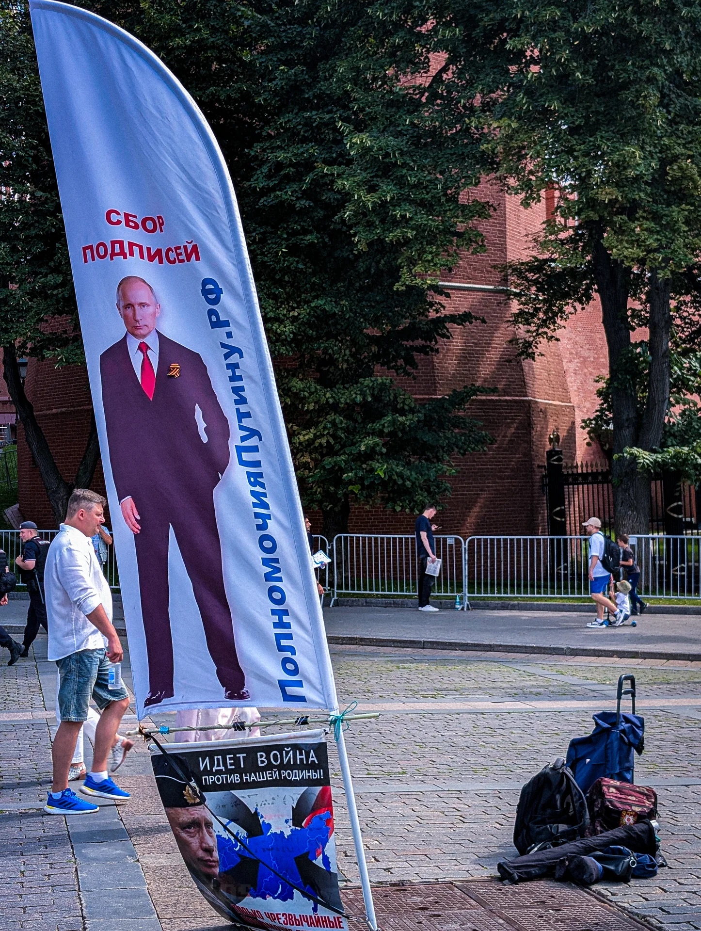 Вертикальный белый флаг-стенд с политической агитацией и надписями на городской площади в окружении людей.